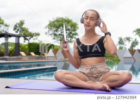 Non-binary person exercising in poolside doing yoga and wearing sport bra 127942984
