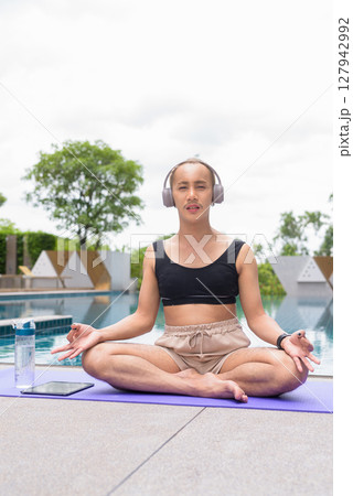 Non-binary person exercising in poolside doing yoga and wearing sport bra 127942992