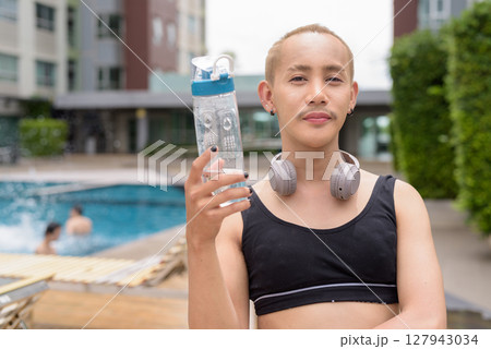 Non-binary person relaxing in poolside during summer wearing sport bra Non-binary person relaxing in poolside during summer wearing sport bra 127943034