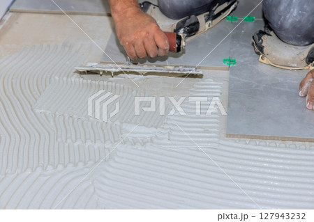 Worker skillfully spreads tile adhesive on floor surface for home renovation project. 127943232