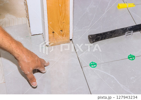 Hand of worker aligns tiles on floor while preparing for next step in home renovation. 127943234