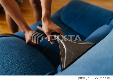 Cleaning service employee vacuuming blue upholstery, removing stubborn dirt and eliminating stains for spotless, sanitized furniture surface closeup. Concept of domestic work, housekeeping, household. Cleaning service employee vacuuming blue upholstery, removing stubborn dirt and eliminating stains for spotless, sanitized furniture surface closeup. Concept of domestic work, housekeeping, household. 127943346