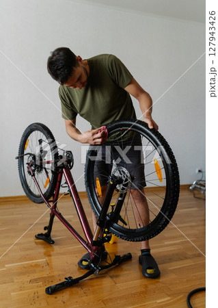 Vertical shot of cyclist male wiping dusty dirty tire of bicycle wheel with cloth, detailing bicycle at home showing commitment to cycling maintenance and equipment care. Concept of bike service Vertical shot of cyclist male wiping dusty dirty tire of bicycle wheel with cloth, detailing bicycle at home showing commitment to cycling maintenance and equipment care. Concept of bike service 127943426