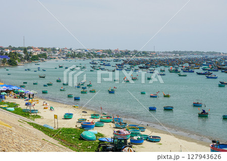 Colorful Fishing Boats Fill the Bay of Mui Ne, Vietnam on a Sunny Day with Bustling Shoreline Market Colorful Fishing Boats Fill the Bay of Mui Ne, Vietnam on a Sunny Day with Bustling Shoreline Market 127943626