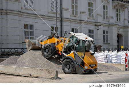 Yellow loader on gravel pile at construction site in front of white building Yellow loader on gravel pile at construction site in front of white building 127943662