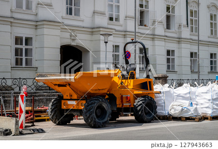 Bright yellow construction dumper truck parked near white building with industrial materials Bright yellow construction dumper truck parked near white building with industrial materials 127943663