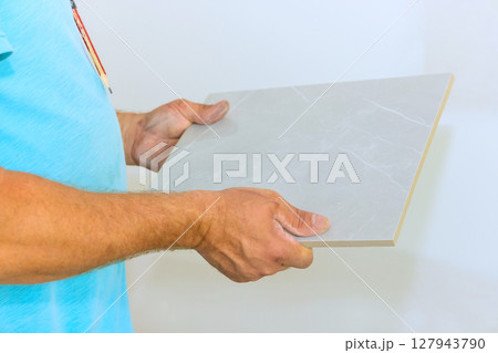 Someone is carefully holding gray tile, ready to be used in home renovation project during works day. 127943790