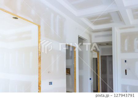 Freshly installed drywall is being prepared in modern home interior with unfinished surfaces open doorways. 127943791