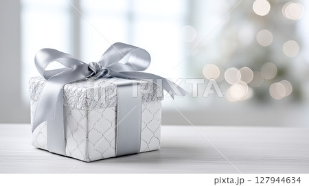 Beautifully wrapped gift box with silver ribbon on a festive table 127944634