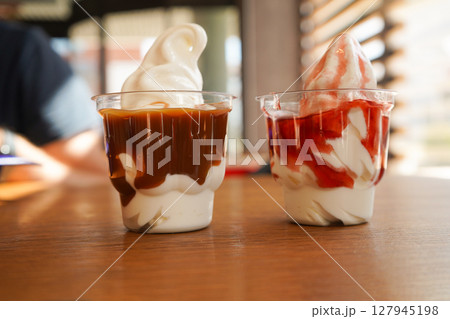 There are two plastic cups containing delicious strawberry and caramel ice cream side by side. 127945198