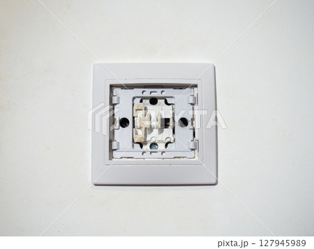 Broken electrical switch on the wall. Switch without button. Disassembled device. White wall with electric light switch. Appliances. 127945989