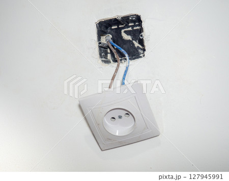 Broken electrical socket on the wall. Disassembled device. White wall with a socket pulled out of the wall. Life threatening. Broken electrical equipment concept. Appliances. Wires out. 127945991