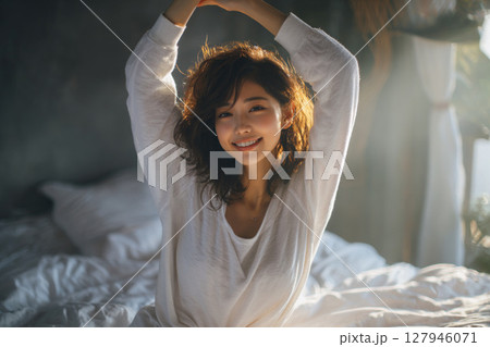 朝日差し込むベッドで微笑む若い女性の寝起きのひととき 朝日差し込むベッドで微笑む若い女性の寝起きのひととき 127946071