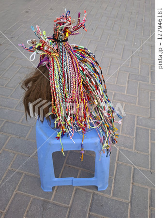 Intricate African braiding patterns are showcased on a blue stool in a vibrant Spanish resort town, capturing the essence of cultural exchange and creativity. Intricate African braiding patterns are showcased on a blue stool in a vibrant Spanish resort town, capturing the essence of cultural exchange and creativity. 127946181