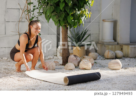 Woman preparing mat outdoors for yoga pilates or stretching practice fitness wellness routine healthy active lifestyle. 127949493