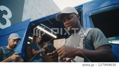 Loader Using Smartphone, Diverse Workers Loading Delivery Truck with Cardboard Boxes Loader Using Smartphone, Diverse Workers Loading Delivery Truck with Cardboard Boxes 127949630