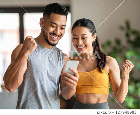 スマホを見ながら筋肉の成長を喜びあう20代日本人男性と女性 127949983