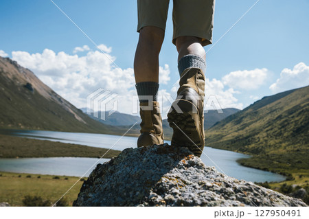 Hiker legs wearing leather boots hiking on high altitude mountain top,with a lake in the distance 127950491