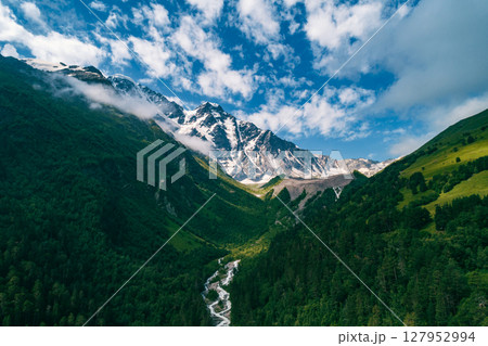 Majestic snow-capped Caucasus mountains rise above lush green valleys and a winding river on a sunny day in the wilderness Majestic snow-capped Caucasus mountains rise above lush green valleys and a winding river on a sunny day in the wilderness 127952994