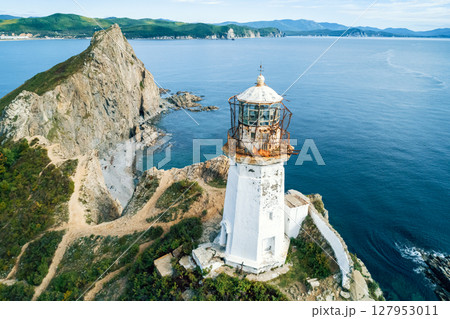 A weathered lighthouse stands on a rugged cliff, overlooking a vast ocean. A weathered lighthouse stands on a rugged cliff, overlooking a vast ocean. 127953011