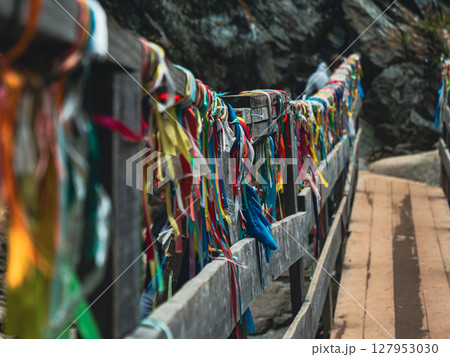 Colorful ribbons adorn a wooden bridge leading to a rocky landscape in a serene outdoor setting Colorful ribbons adorn a wooden bridge leading to a rocky landscape in a serene outdoor setting 127953030
