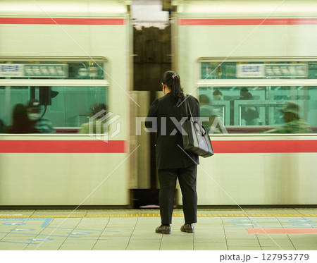 駅のホームで電車待ちの若い女性会社員と通過中の電車の風景 127953779