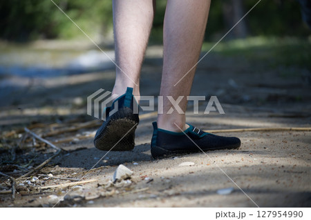 Person walking on a sandy path wearing minimal black shoes in nature. 127954990