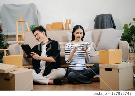 Asian young attractive couple man and woman use tablet and smartphone online shopping furniture decorate house with carton package move in new house. 127955748