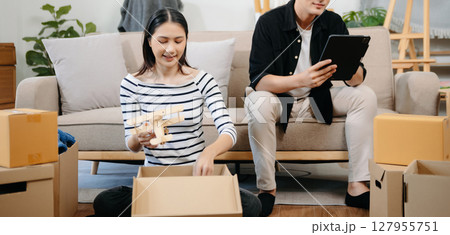 Asian young attractive couple man and woman use tablet and smartphone online shopping furniture decorate house with carton package move in new house. 127955751