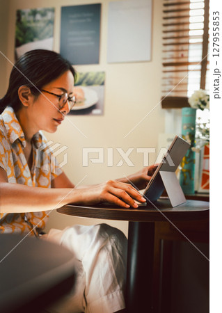 Asian woman working with a laptop sitting at a cafe table. 127955853