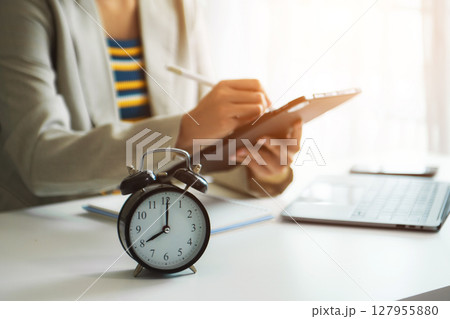 Alarm clock on the desk. Business hand using smartphone, laptop and tablet  working in modern office building 127955880