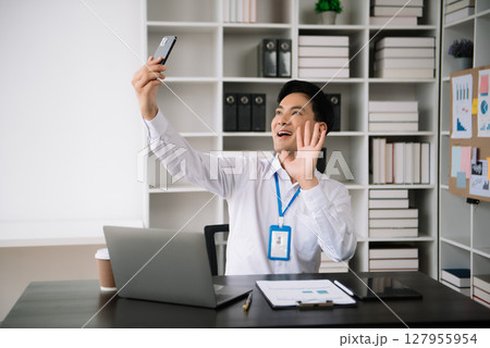 Young Asian business man using laptop and tablet while sitting at her working place. Concentrated at work. 127955954