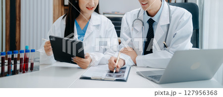 Medical team having a meeting with doctors in white lab coats and surgical scrubs seated at a table discussing a patients working online using computers in the medical industry Medical team having a meeting with doctors in white lab coats and surgical scrubs seated at a table discussing a patients working online using computers in the medical industry 127956368
