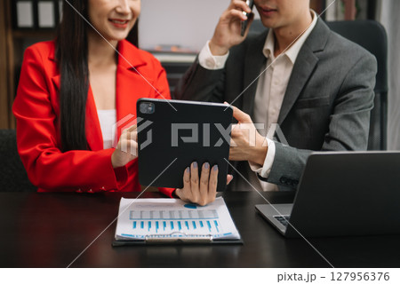 Asian business colleague business presents and explains and using laptop and tablet. Teamwork, financial marketing team,   while sitting in modern office 127956376