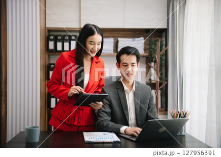Asian business colleague business presents and explains and using laptop and tablet. Teamwork, financial marketing team, while sitting in modern office Asian business colleague business presents and explains and using laptop and tablet. Teamwork, financial marketing team, while sitting in modern office 127956391