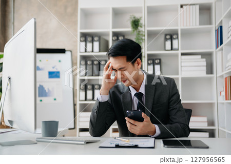 Asian businessman is stressed, bored, and overthinking from working on a tablet at the office. Asian businessman is stressed, bored, and overthinking from working on a tablet at the office. 127956565