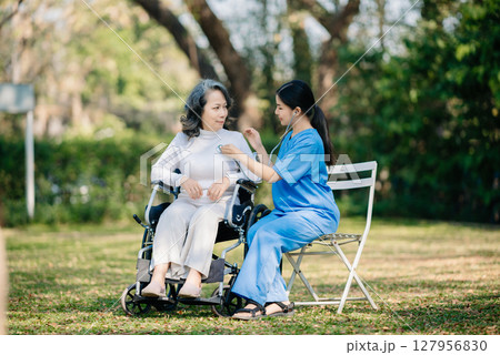 Elderly asian senior woman on wheelchair with Asian careful caregiver. Nursing home hospital garden Elderly asian senior woman on wheelchair with Asian careful caregiver. Nursing home hospital garden 127956830