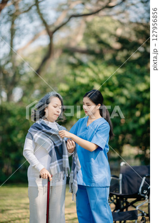 Asian young caregiver nurse support senior older male walking outdoors. Specialis doctor help and take care of elderly mature. Nursing home hospital garden 127956856