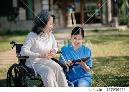Asian young caregiver nurse support senior older male walking outdoors. Specialis doctor help and take care of elderly mature. Nursing home garden concept. Asian young caregiver nurse support senior older male walking outdoors. Specialis doctor help and take care of elderly mature. Nursing home garden concept. 127956933