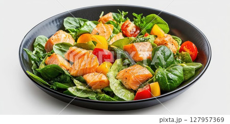 Fresh spinach salad with grilled salmon and colorful vegetables served in a black bowl on a white background 127957369