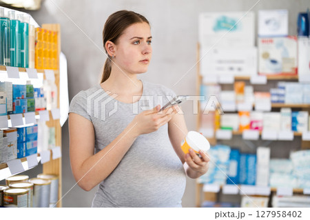 Pregnant woman scans QR code on skin cream label in pharmacy Pregnant woman scans QR code on skin cream label in pharmacy 127958402