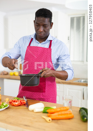 Smiling adult man in red apron preparing vegetable dish in home kitchen 127958403