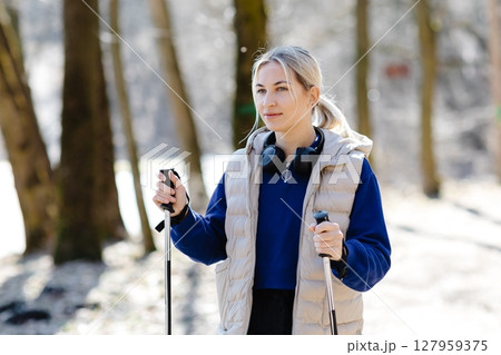 Young woman nordic walking in forest during winter sunny day 127959375