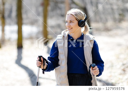 Young Woman Nordic Walking in Forest Listening Music with Headphones 127959376