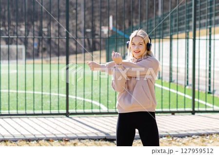 Young sporty woman stretching arm outdoors wearing headphones and smiling Young sporty woman stretching arm outdoors wearing headphones and smiling 127959512