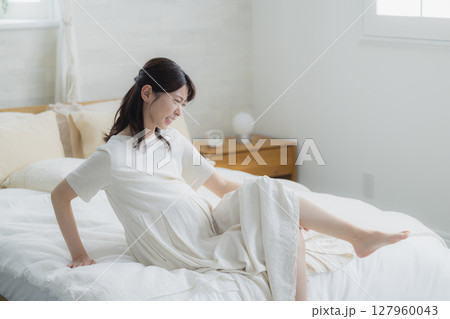 寝室でベッドに座る足が攣った女性 127960043