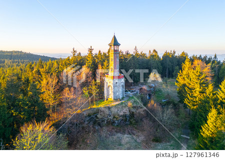Stepanka Lookout Tower rises majestically in Korenov, surrounded by lush greenery of the Jizera Mountains. A calm spring morning reveals its charming architecture under clear skies. Stepanka Lookout Tower rises majestically in Korenov, surrounded by lush greenery of the Jizera Mountains. A calm spring morning reveals its charming architecture under clear skies. 127961346