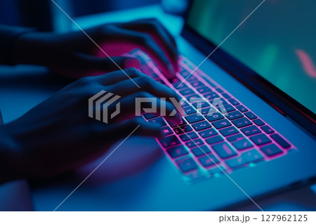 Close-up of fingers typing on vibrant pink and blue illuminated keyboard at night 127962125