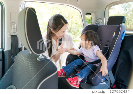 子供をチャイルドシートに座らせるママ 127962424