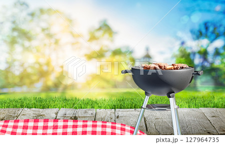 charcoal barbecue grill with open flame, chicken meat, backyard and wooden table with red tablecloth 127964735